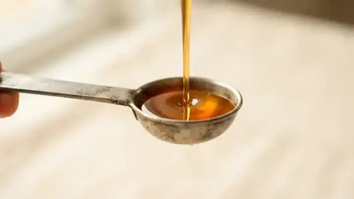 A tin measuring spoon filling with glowing golden amber herbal syrup, close-up, slow camera move